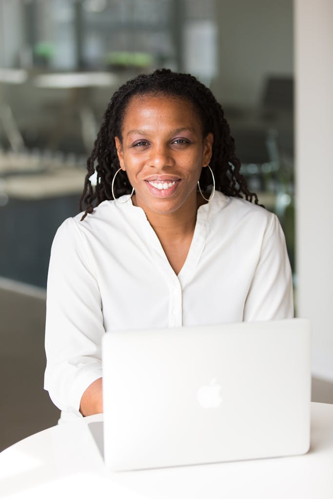 Confident woman smiling while sitting at an office desk with a laptop, showcasing a positive work environment.